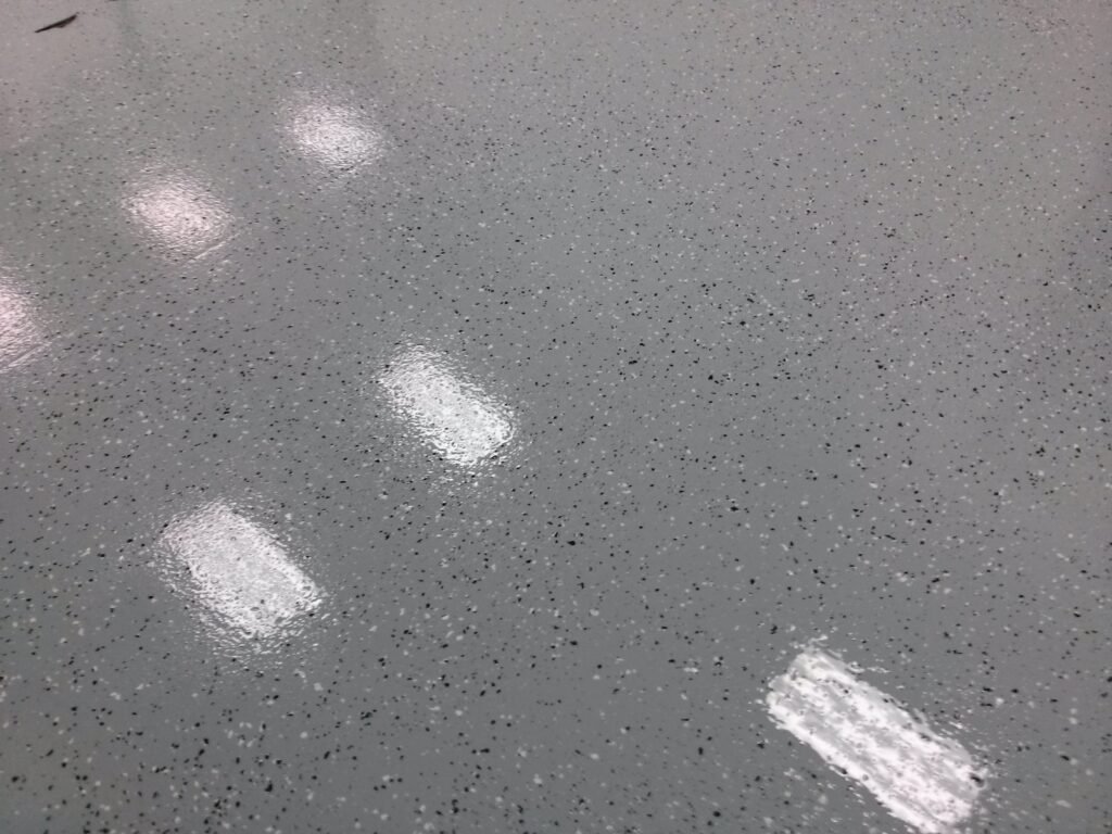 Close up image of a polyaspartic gray concrete chip floor with the reflective overhead lights.