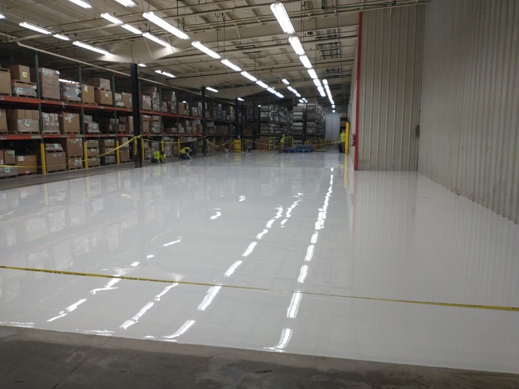 White polyaspartic concrete coating completed in a manufacturing plant in Wisconsin showing reflectivity of overhead lighting and a smooth and visually appealing appearance.