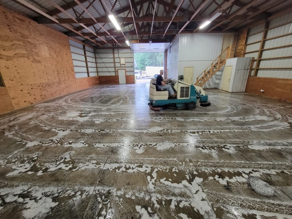 Industrial floor cleaning taking place in Montello, Wisconsin showing a rideable sweeper scrubber machine.