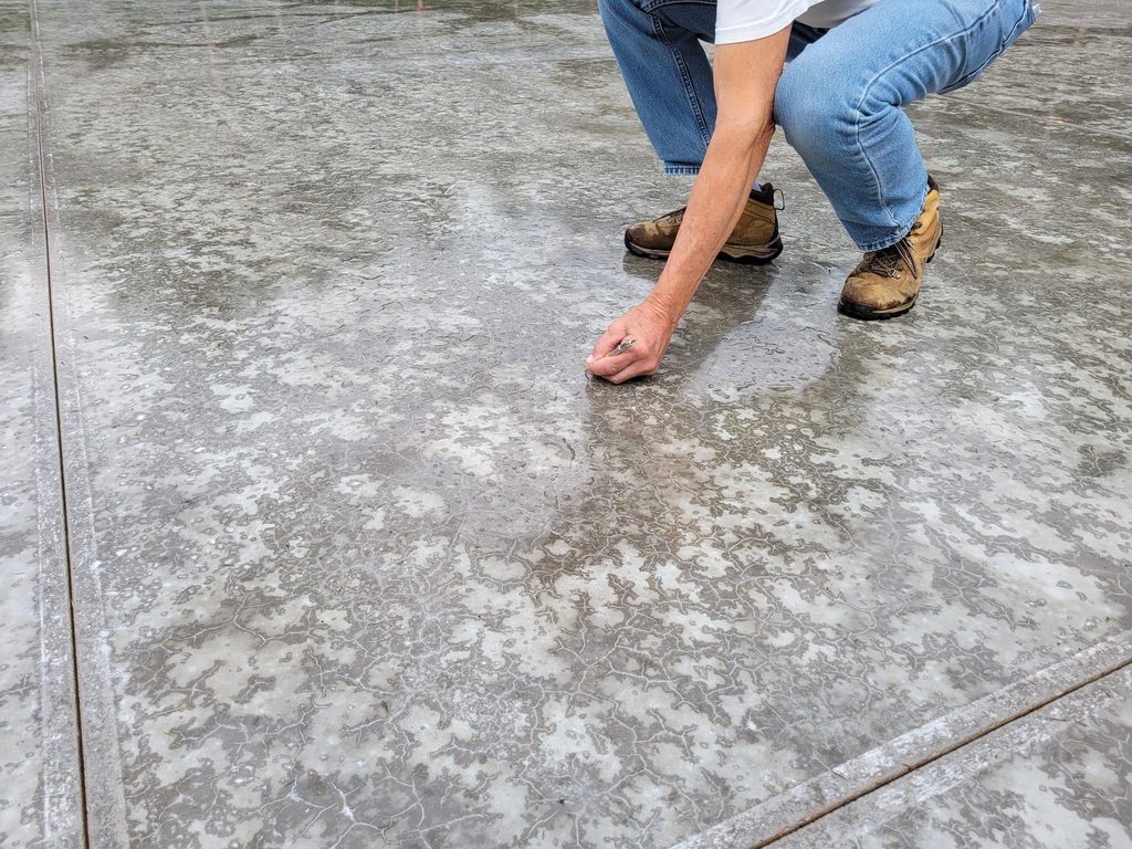 A concrete specialist testing the hardness of a slab of concrete using the Mohs harness scratch test.